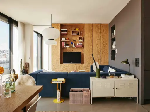 Un salón moderno con sofá azul, estanterías de madera y lámparas colgantes. Un espacio acogedor para **tini living**.