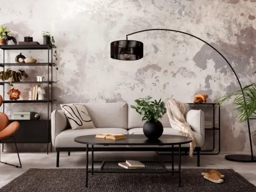 Sofá gris, mesa negra y estantería metálica en una sala con decoración estilo industrial chic. Pared texturizada y silla naranja.