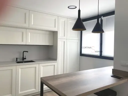Cocina moderna con armarios blancos, encimera gris, grifo negro y cortinas blancas. Ideas para tu cocina.