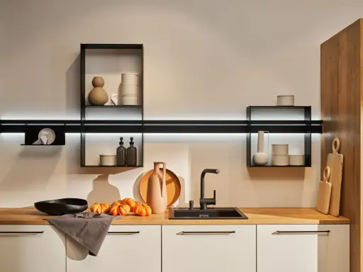 Cocinas sin muebles altos, con estantes flotantes y decoración minimalista. Encimera de madera con fregadero negro, jarrones y calabazas.