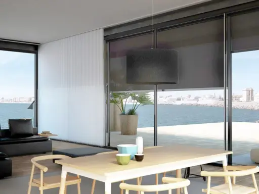 Comedor moderno con vistas al mar, decorado con estores Bandalux que controlan la luz.