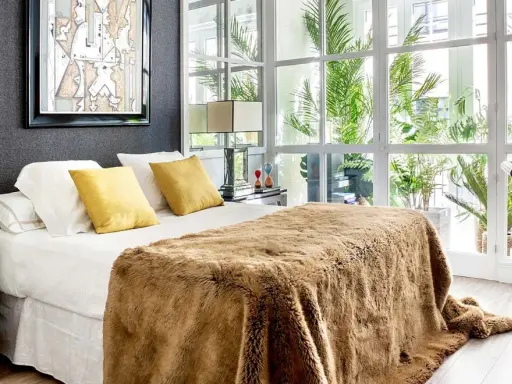 Cama acogedora con manta peluda, cojines amarillos y arte abstracto. Un diseño moderno para decorar habitación con luz natural.