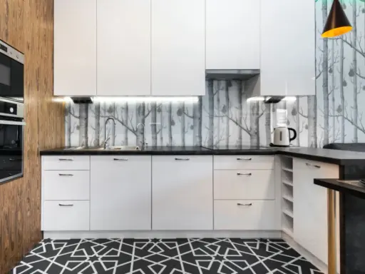 Cocinas modernas con papel pintado de árboles, gabinetes blancos y suelo geométrico.
