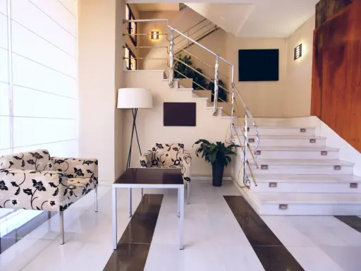 Elegante rellano escalera decoracion con sillones florales y una lámpara de pie. El descansillo escalera cuenta con una barandilla metálica y luces integradas.