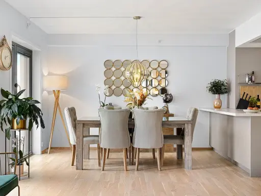 Comedor elegante con mesa de madera y sillas tapizadas, sobre un suelo sisal. Decoración con espejos circulares y lámpara colgante.