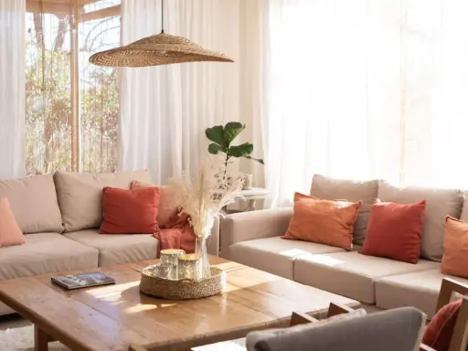 Salones pequeños con encanto: sofás beige, cojines terracota y naranja, mesa de madera, plantas y luz natural.
