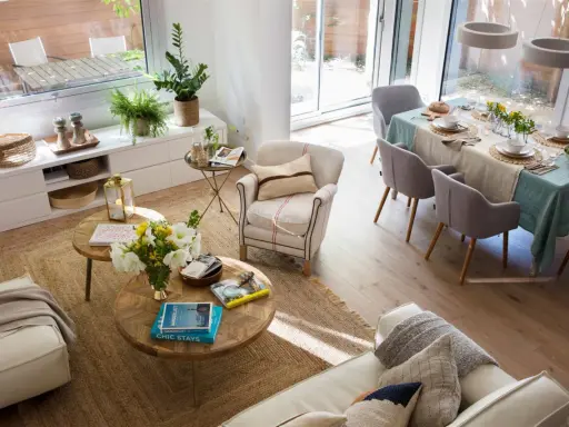 Espacio luminoso con sofás, mesas de centro y una mesa de comedor lista para una comida. La distribución del comedor es funcional y acogedora.