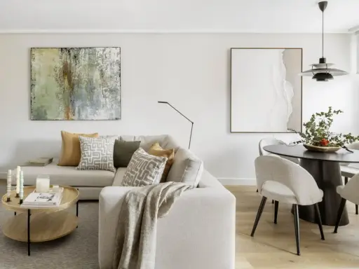 Salones con colores neutros: sofá beige, mesa de centro de madera, cuadros abstractos y mesa de comedor con sillas tapizadas.