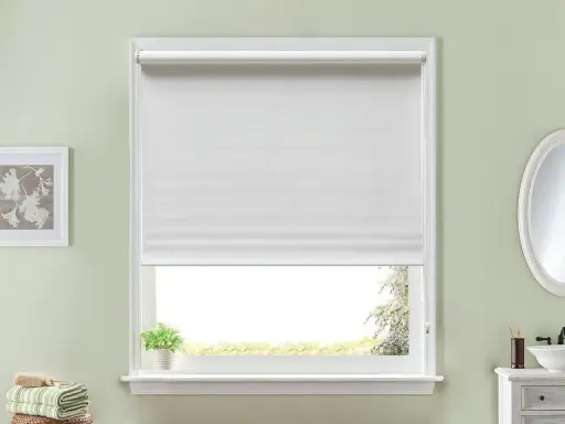 Persiana enrollable blanca que cubre la mayor parte de la ventana. Un pequeño paquete de toallas verdes y blancas descansa en la repisa.