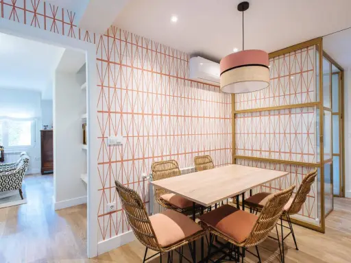Comedor con papel pintado de rombos naranjas, mesa de madera y sillas de mimbre. Un ejemplo de como poner papel pintado para renovar tu hogar.
