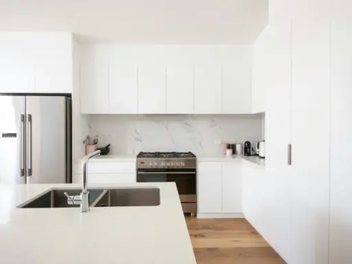 Cocinas blancas elegantes con encimeras de cuarzo, electrodomésticos de acero inoxidable y suelo de madera.