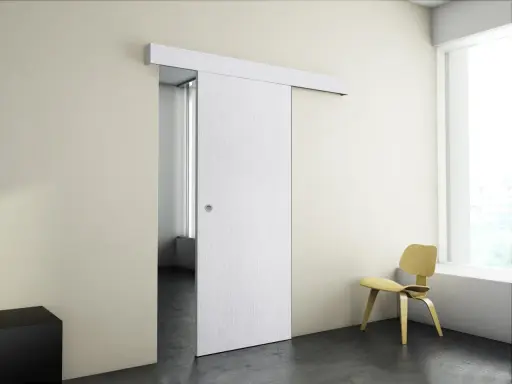 Puerta corredera blanca moderna instalada en pared beige, con silla amarilla y ventana al fondo.