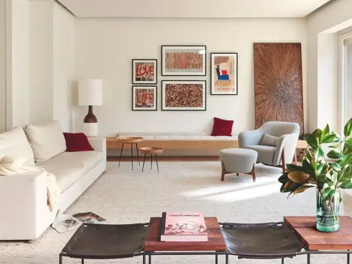 Una composición de cuadros en la pared, con arte abstracto y tipografía, decora este salón moderno junto a un sofá blanco y una butaca gris.