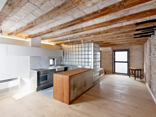 Cocina moderna con isla de madera y cristal, techos de vigas expuestas. Un espacio abierto que evoca la idea de como tirar un tabique para crear amplitud.