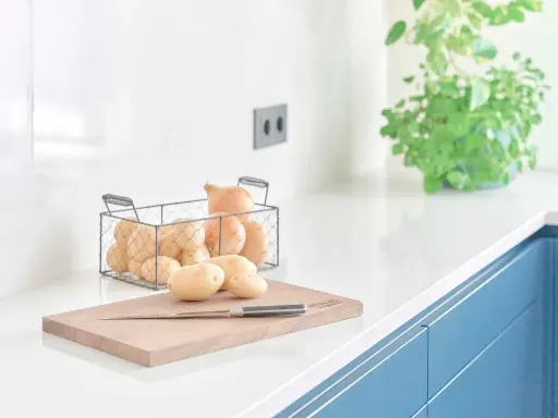 Encimeras de cocina blancas y lisas, con patatas y cebollas listas para cocinar.