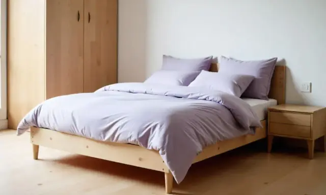 Cama con funda nórdica Bassols en tono lavanda, almohadas a juego, mesita de noche de madera y armario.