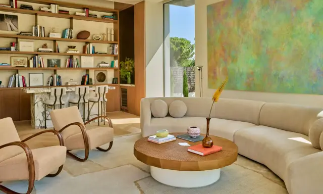 Sofá curvo y sillones de diseño contemporáneo, estanterías llenas de libros y arte abstracto en un salón luminoso.