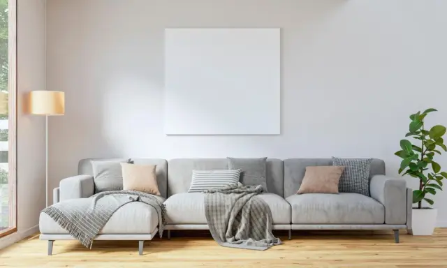 Un sofá gris moderno, listo para decorar con cojines y mantas, junto a una lámpara y una planta.