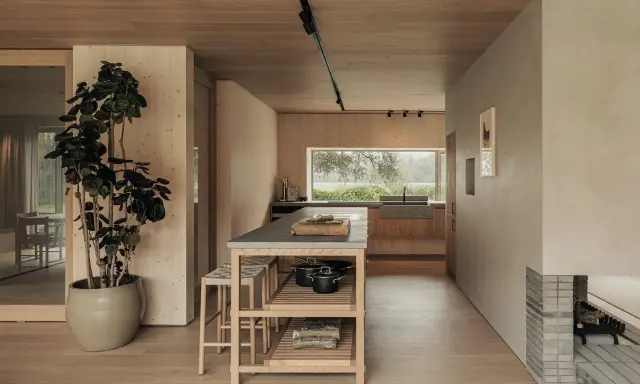 Un acogedor salón cocina pequeño con isla central, mucha madera y una gran ventana al exterior.