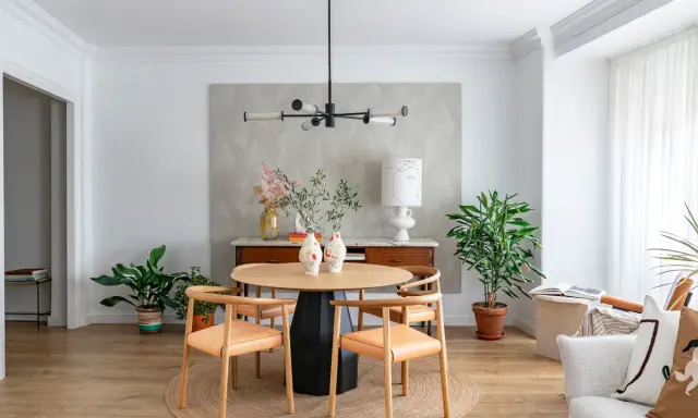Comedor con mesa redonda de madera, sillas de cuero, lámpara moderna y plantas. Ideal para decorar piso moderno y elegante.