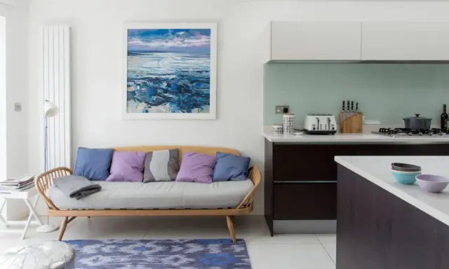 Acogedora cocina con un cómodo sofá de madera y cojines coloridos, junto a una isla y un cuadro de paisaje marino.