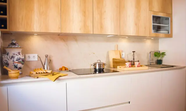 Cocina blanca y madera con encimera de mármol. Hay pan, huevos, una olla y una planta.