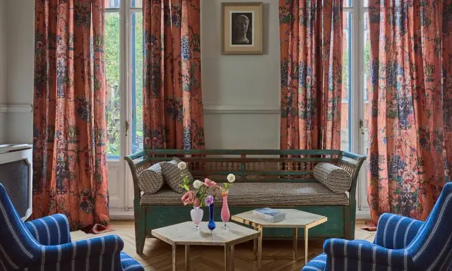 Cortinas de lino estampado con motivos florales y botánicos en tonos anaranjados, complementando un sofá vintage y sillones a rayas.