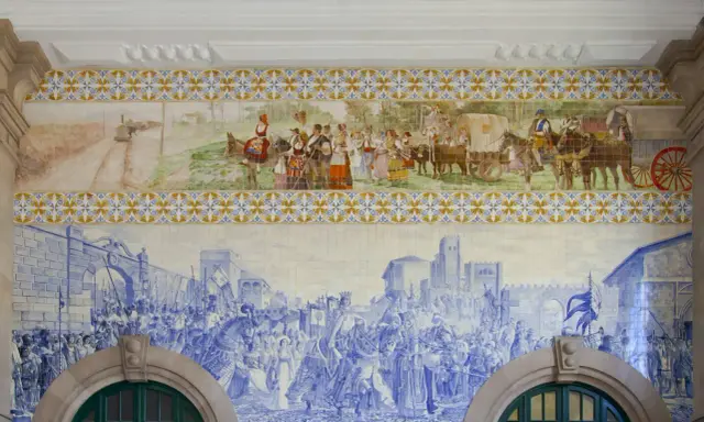 Azulejos de Oporto narran la historia: un tren antiguo, gente vestida de época y una procesión militar en azul y blanco.