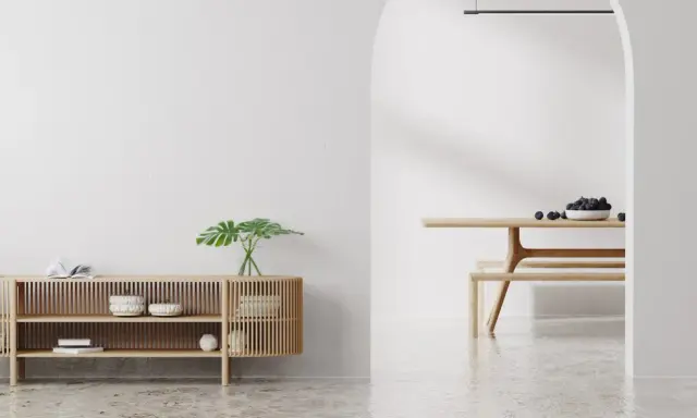 Un espacio minimalista con un aparador de madera y un comedor. Las paredes lisas y el suelo pulido crean un ambiente sereno.