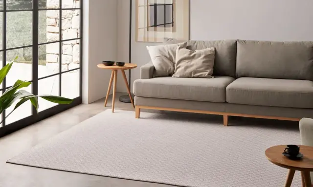 Elegante salón con sofá gris y alfombra de patrones geométricos, mostrando diversos tipos de alfombras para un hogar acogedor.