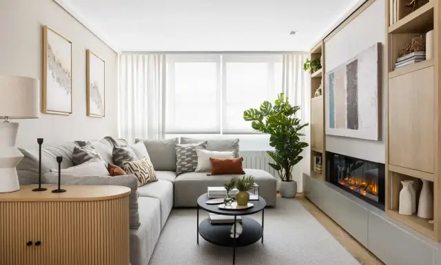 Acogedora decoracion salon pequeño con sofá gris, chimenea moderna y estanterías de madera.
