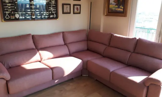 Cómodo sofá rinconera rosa, ideal para decorar salón. En la pared, un cuadro de nudos marineros y pinturas.