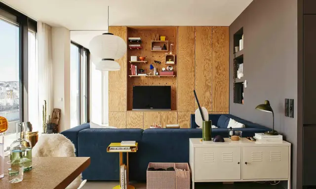 Un salón moderno con sofá azul, estanterías de madera y lámparas colgantes. Un espacio acogedor para **tini living**.