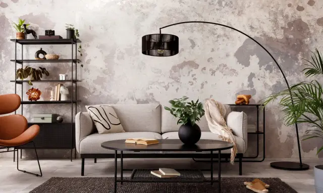 Sofá gris, mesa negra y estantería metálica en una sala con decoración estilo industrial chic. Pared texturizada y silla naranja.