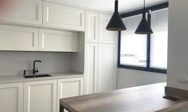 Cocina moderna con armarios blancos, encimera gris, grifo negro y cortinas blancas. Ideas para tu cocina.