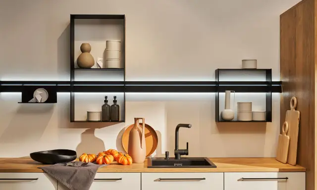 Cocinas sin muebles altos, con estantes flotantes y decoración minimalista. Encimera de madera con fregadero negro, jarrones y calabazas.