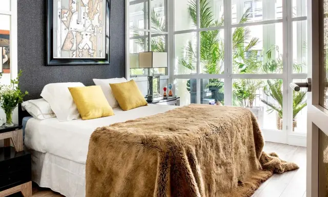Cama acogedora con manta peluda, cojines amarillos y arte abstracto. Un diseño moderno para decorar habitación con luz natural.
