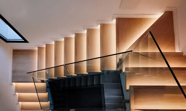 Moderna escalera de madera con iluminación indirecta y barandillas de cristal, vistas en el salón.