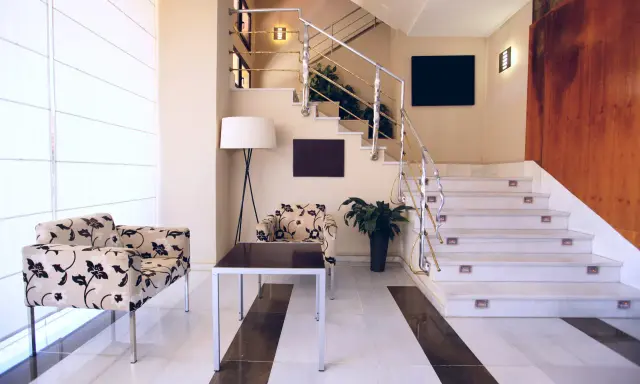 Elegante rellano escalera decoracion con sillones florales y una lámpara de pie. El descansillo escalera cuenta con una barandilla metálica y luces integradas.