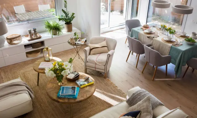Espacio luminoso con sofás, mesas de centro y una mesa de comedor lista para una comida. La distribución del comedor es funcional y acogedora.