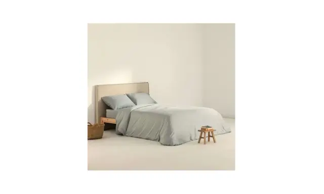 Cama con funda nordica 180x220 en tono gris claro, almohadas a juego y una cesta de mimbre al lado.