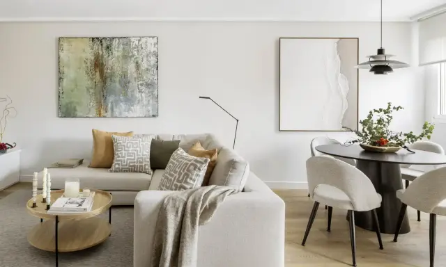Salones con colores neutros: sofá beige, mesa de centro de madera, cuadros abstractos y mesa de comedor con sillas tapizadas.