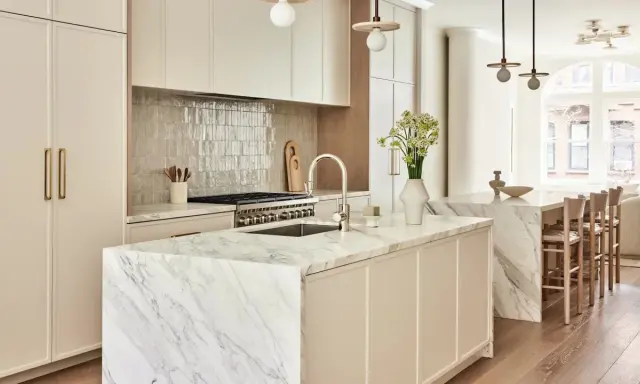 Elegante cocina atemporal con isla de mármol, gabinetes crema y electrodomésticos de acero inoxidable. Un jarrón con flores ilumina el espacio.