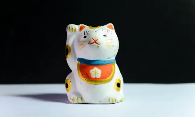 Maneki-neko blanco con detalles dorados y flor, ideal para feng shui en casa para la prosperidad.