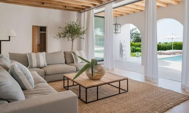 Sofá gris, mesa de centro de madera y alfombra de yute en un salón luminoso con vistas a una piscina.