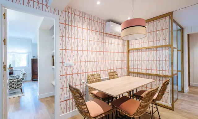 Comedor con papel pintado de rombos naranjas, mesa de madera y sillas de mimbre. Un ejemplo de como poner papel pintado para renovar tu hogar.