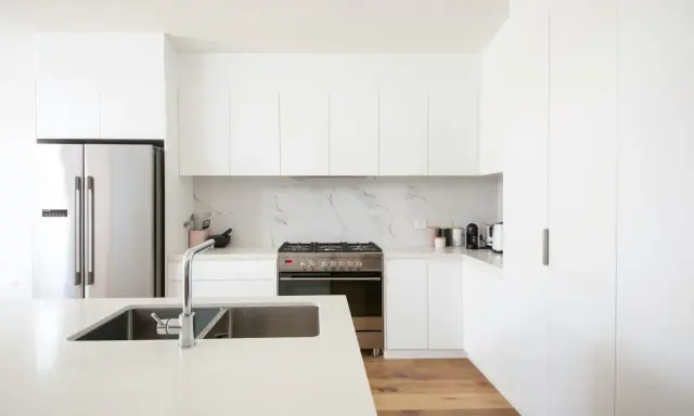 Cocinas blancas elegantes con encimeras de cuarzo, electrodomésticos de acero inoxidable y suelo de madera.