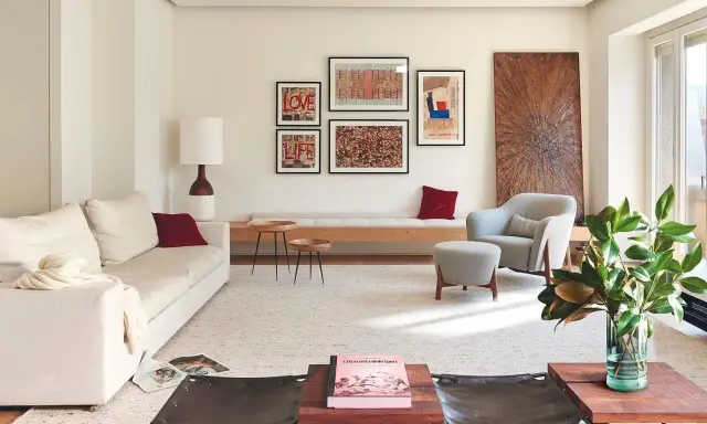 Una composición de cuadros en la pared, con arte abstracto y tipografía, decora este salón moderno junto a un sofá blanco y una butaca gris.