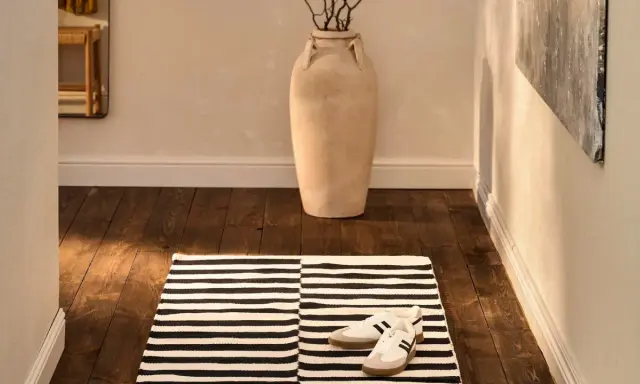 Alfombra pasillero a rayas blancas y negras, con zapatillas deportivas y un jarrón grande.
