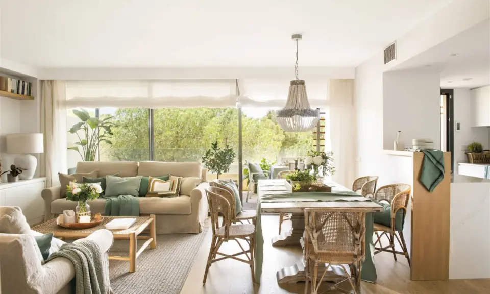 Elegante decoracion salon con sofás, mesa de comedor de madera, sillas de mimbre y gran ventanal con vistas al exterior.